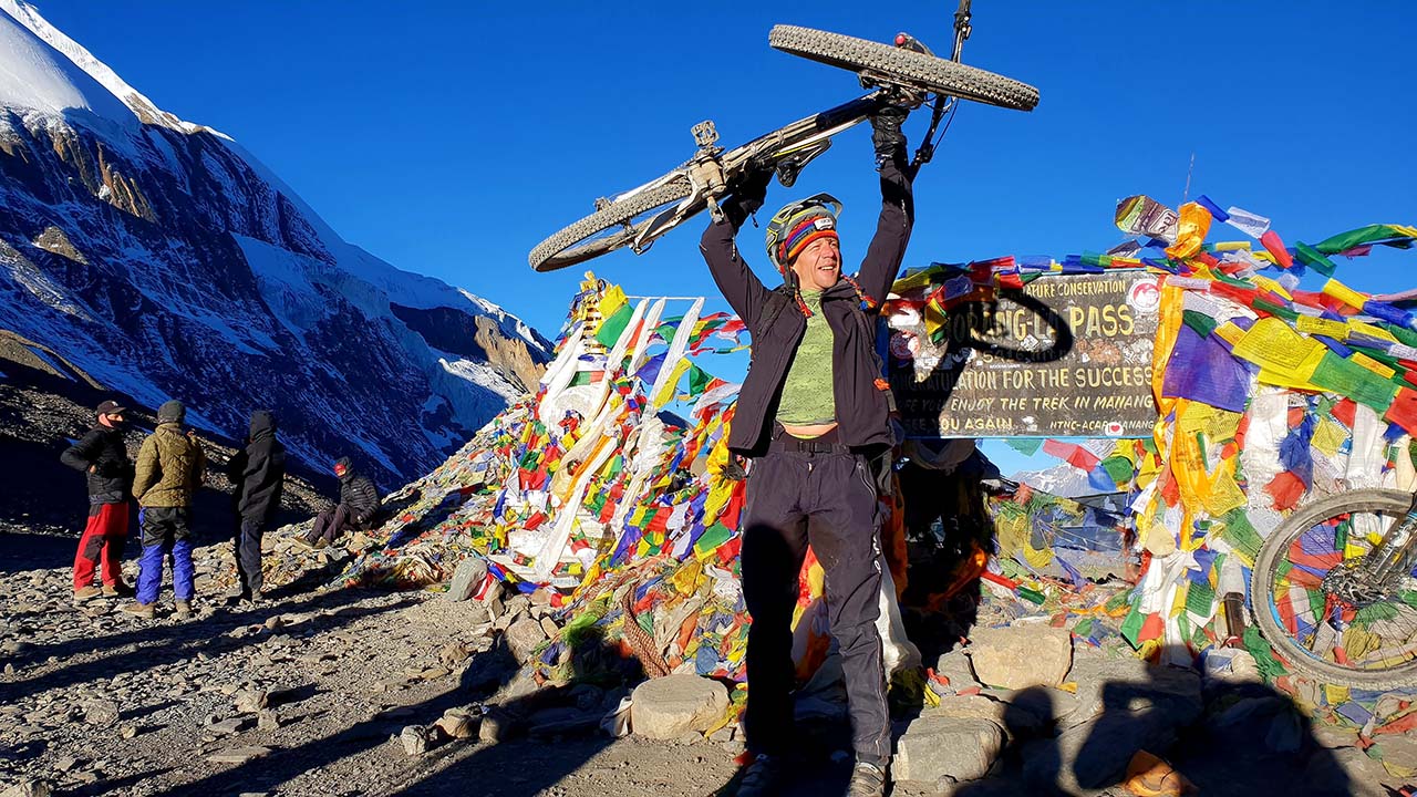 A happy mountain biker lifting the bike over Thorong-La Pass during Nepal Annapurna Circuit MTB Tour.